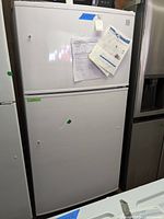 Full view of the Kenmore white top freezer refrigerator with documents taped on the door.