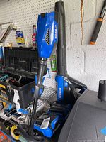 Two blue Kobalt garden tools standing on floor with two chargers and batteries visible