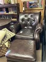 Brown leather arm chair and matching ottoman, showing front view with tufted backrest and cushioned ottoman.
