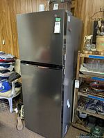 Front view and surroundings of LG refrigerator with top freezer, metallic gray finish, showing top freezer door and larger fridge door below.