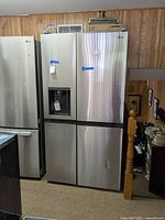 Full view of stainless steel four-door refrigerator with taped right door and water dispenser on left door