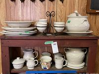 Longaberger Pottery serving pieces arranged on a wooden console table, showing soup tureens, creamers, mugs, and bowls.