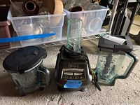 Full view of the Ninja blender base with two different blending jars and one blending attachment jar surrounding the base. The jars are glass and have lids and handles.
