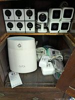 Photo of Orbi wireless router and eleven Wyze Cam v2 cameras with cables and power adapters inside a wooden cabinet