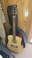 Full view of Peavey acoustic guitar standing against a wall with soft case behind it.