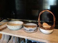Three pottery pieces and hand brush grouped together on wooden shelf beneath TV