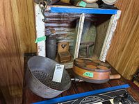 Full view of primitive wooden cupboard with vintage kitchenware inside including metal scoop, long pan, wooden spice set, and match box holder.