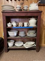 Front view of primitive painted wood cabinet showing three shelves with various dishware (not included). Cabinet has red painted finish, visibly worn and soiled.