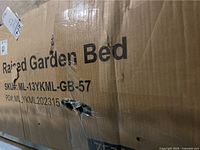 Close up photo of front of cardboard box showing 'Raised Garden Bed' and SKU ML-13YKML-GB-57 with holes and damage to box surface