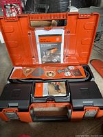 Fein MultiMaster tool kit in open orange hard case showing manual, attachments, and tool compartments