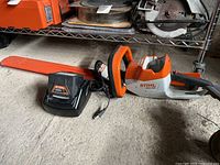Overview of hedge trimmer, battery inserted, charger adjacent