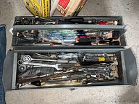 Top view of the metal toolbox with two compartments filled with assorted hand tools including wrenches, ratchets, sockets, and screwdrivers.
