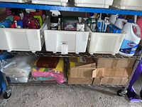 Bottom shelf of metal shelving showing cardboard boxes containing generic trash bags and folded cleaning rags.