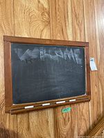 Wood framed chalkboard with visible scratches and some chalk writing, placed on wooden floor.