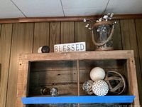 Wooden shelf displaying the 'Blessed' sign, glass bucket with faux flowers, decorative balls, and some door knobs on the bottom shelf.