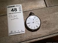 Front view of vintage pocket watch showing white dial with Roman numerals and minute and hour hands along with a sub-seconds dial at 6 o'clock. Case shows patina and normal wear.