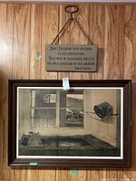 Wide shot of the framed black and white print and the hanging motivational plaque on a wood-paneled wall