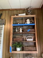 Full view of wooden wall mounted shelf fastened to wooden paneled wall with decorative items inside compartments (not included).