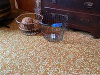 Two vintage wire baskets and three organic decorative balls on carpeted floor.
