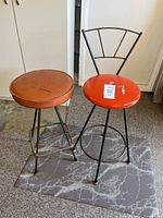 Two retro metal stools placed side-by-side on a gray patterned mat in a garage setting.