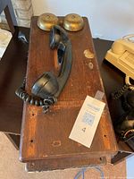 Vintage wooden wall-mounted telephone showing two brass bells, black handset, and coiled cord on dark wooden box with wear marks.