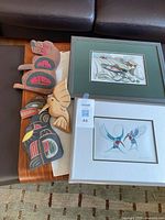 Photo of two carved wooden Indigenous sculptures and two framed Indigenous art prints on a table under natural light showing details and colors