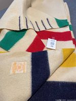 Folded cream wool blanket showing green, red, yellow and navy stripes along with visible woven label.