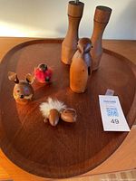 Seven teak wooden items on a tray including 2 grinders, 1 bird whistle, and 4 animal figures with fur accents and red eyes.