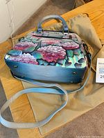 Leather purse with hand-painted floral design from the side showing the base and shoulder strap.