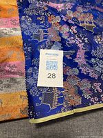 Fabric with maxsold tag '28' showing part of the blue and gold border with intricate patterns and suspected silk brocade material.