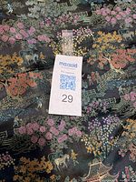 Close-up of black brocade fabric showing intricate multicolor woven Asian landscape design including pagodas, trees, people, horses, and bridges