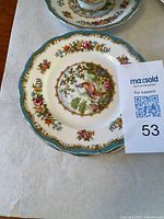 Close-up of a side plate showing floral and bird design with turquoise and gold accents.