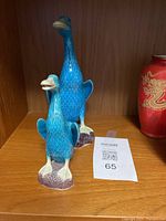 Two blue ceramic duck figurines displayed on wood shelf, showing visible injuries on both.