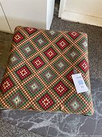 Top close-up photo showing the colorful needlepoint upholstery with diamond patterns in green, red, beige, blue.