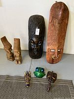 Full lot showing two large wooden masks standing upright, two smaller wooden statues to the left and three small masks including a green frog and brown elephant at front