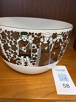 Side view showing ceramic bowl with brown and black folk art figures and floral patterns on white background