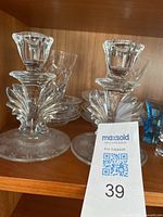 Two decorative crystal candle holders with leaf-like molded glass design on a shelf