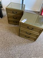 Two wicker look wooden nightstands placed on carpeted floor with visible glass tops and three drawers each.