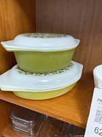 Two yellow-green Pyrex casserole dishes stacked with white lids featuring a green leaf motif pattern.