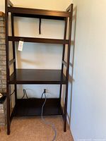 Front view of the dark brown wooden shelf unit showing its three main shelves and top shelf area, with an AC power cable running at the bottom.