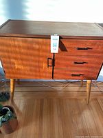 Front view showing left door and three drawers on tapered legs.