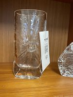 Clear glass Sunburst vase with textured sunburst pattern and central sun motif, cylindrical shape, placed on wooden shelf with MaxSold tag.