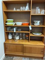 Front view of the teak wall unit cabinet filled with various glassware and kitchenware to show shelving size and placement.
