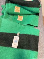 Green Hudson’s Bay wool blanket yardage laid flat on grey surface showing two black stripe groups and sewn-on labels