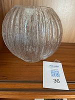 Clear textured rounded glass vase with vertical ribbed pattern, signed TS7, placed on wooden surface next to MaxSold tag 36.