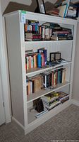 Front view of painted white pinewood bookshelf filled with various books on four adjustable shelves.