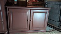 Closed view of the brownish-red painted pinewood cabinet with two doors and round wooden knobs.