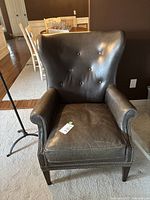 Front view of the grey leather wingback chair showing button tufting and studded edges on armrests.
