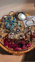 Assorted jewelry items on a wicker/tray surface, including necklaces, bracelets and pins arranged collectively.