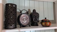 Full view of all four items on a shelf: candle holder, clock, Buddha head statue, and lidded dish.